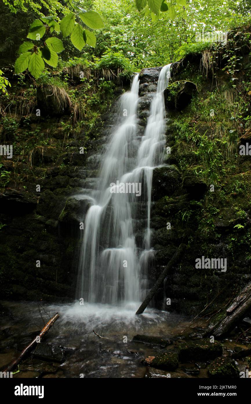 A vertical shot of a waterfall flowing down the rocks covered with ...