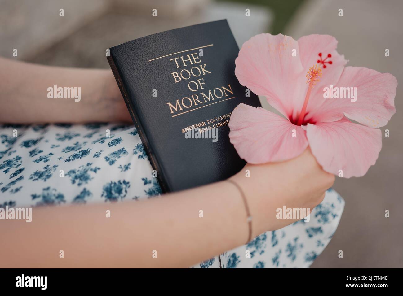 A selective focus shot of a girl holding pink hibiscus and a book Stock Photo