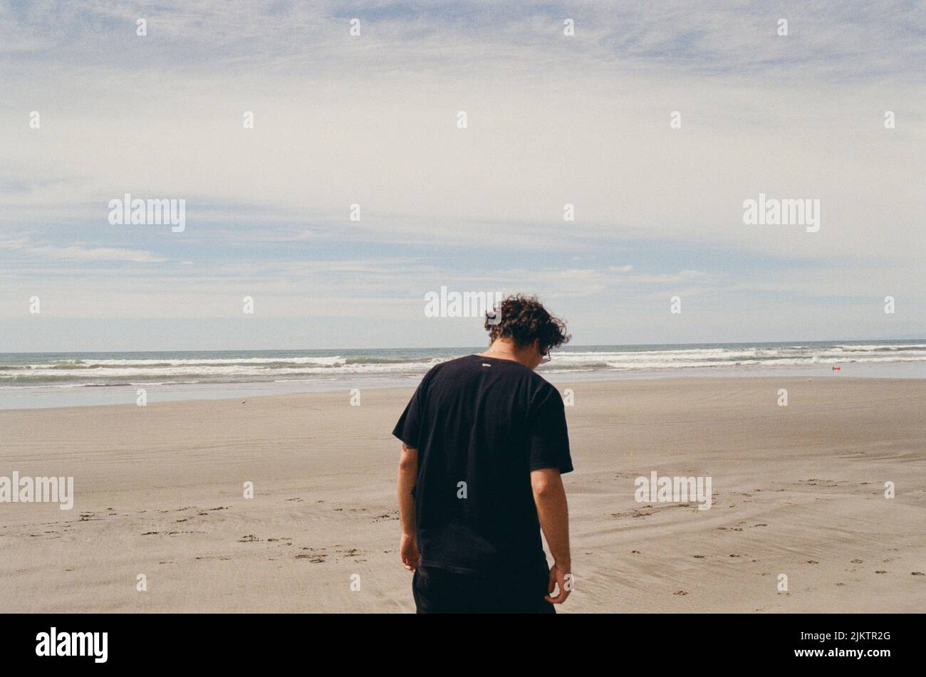 A back view of male with black t-shirt standing on sandy beach in background of sea Stock Photo