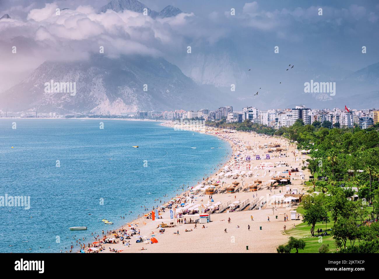 Crowded Antalya city Konyaalti beach with hundreds of vacationers and tourists resting, sunbathing and swimming at extremely hot summer day in resort Stock Photo
