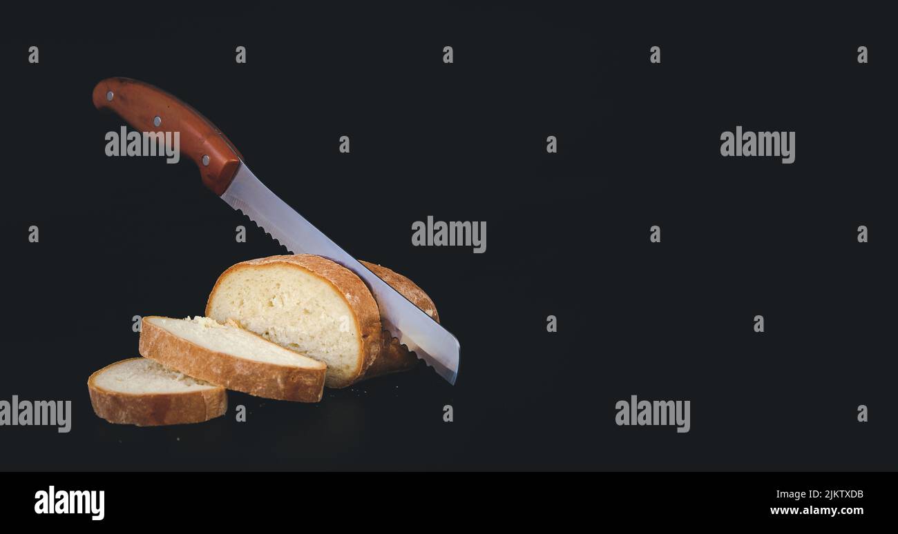 Knife is cutting a loaf of bread into slices. Dark food photo. Rustic style. Selective focus. Toned Stock Photo