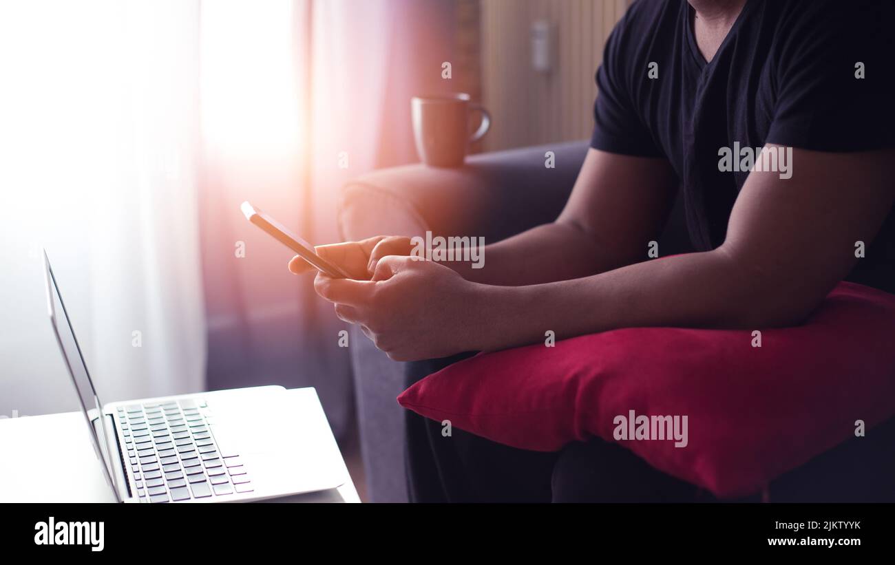 young man at home using his computer and phone having cup of coffee Stock Photo