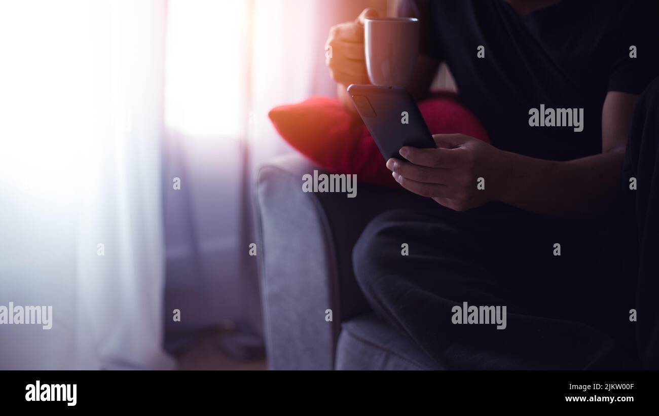 handsome young Hispanic at home drinking coffee and using his smart phone Stock Photo