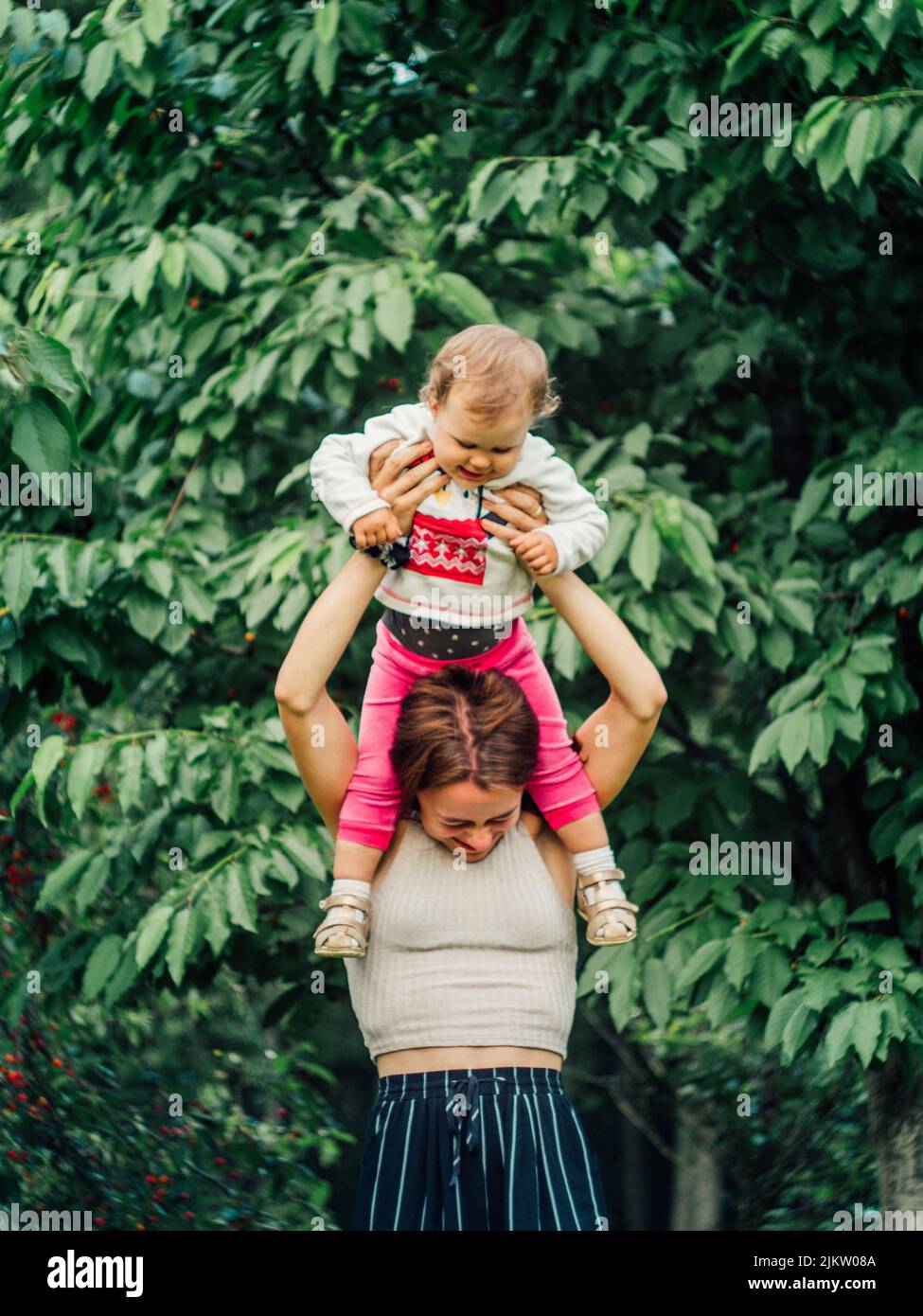 A selective of a happy mother holding up her baby daughter in a park Stock Photo