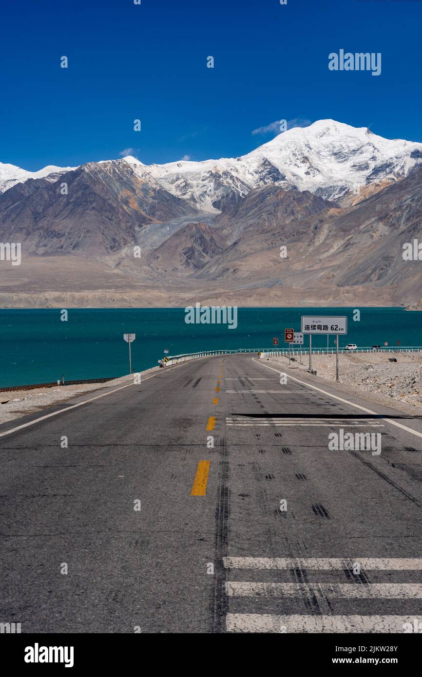 A vertical shot of a waterfront road with mountains in the background