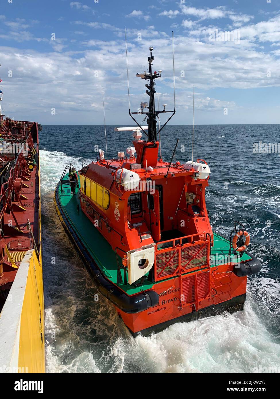 A vertical shot of a pilot boat approaching to a big vessel Stock Photo