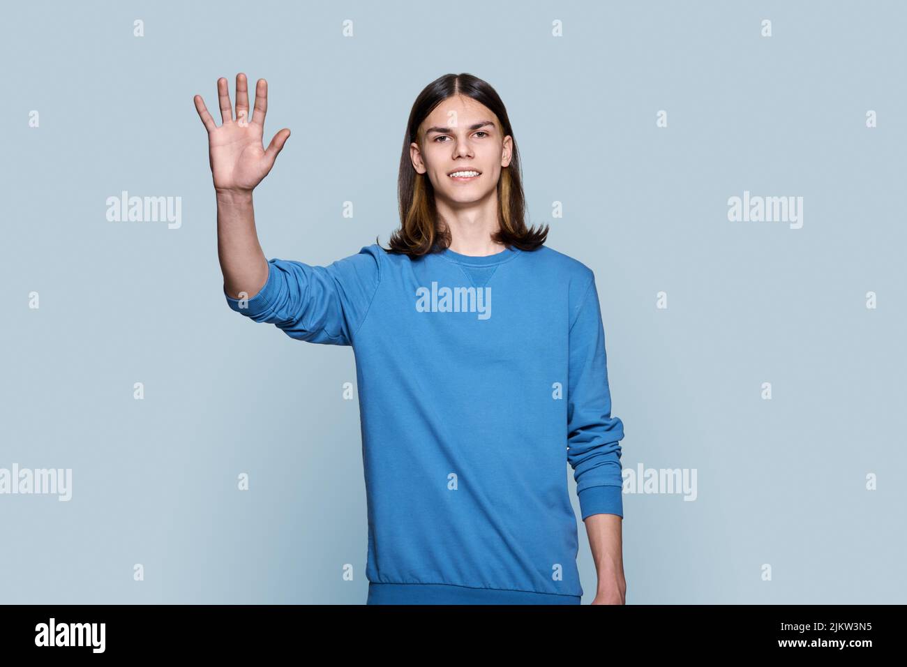 Young guy looking at camera waving his hand, on grey background Stock Photo