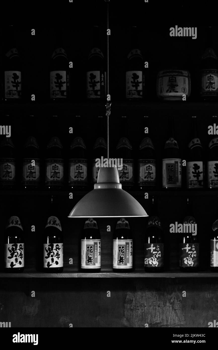 A vertical dramatic shot of a hanging black lamp on a background of bottles with Asian symbols Stock Photo