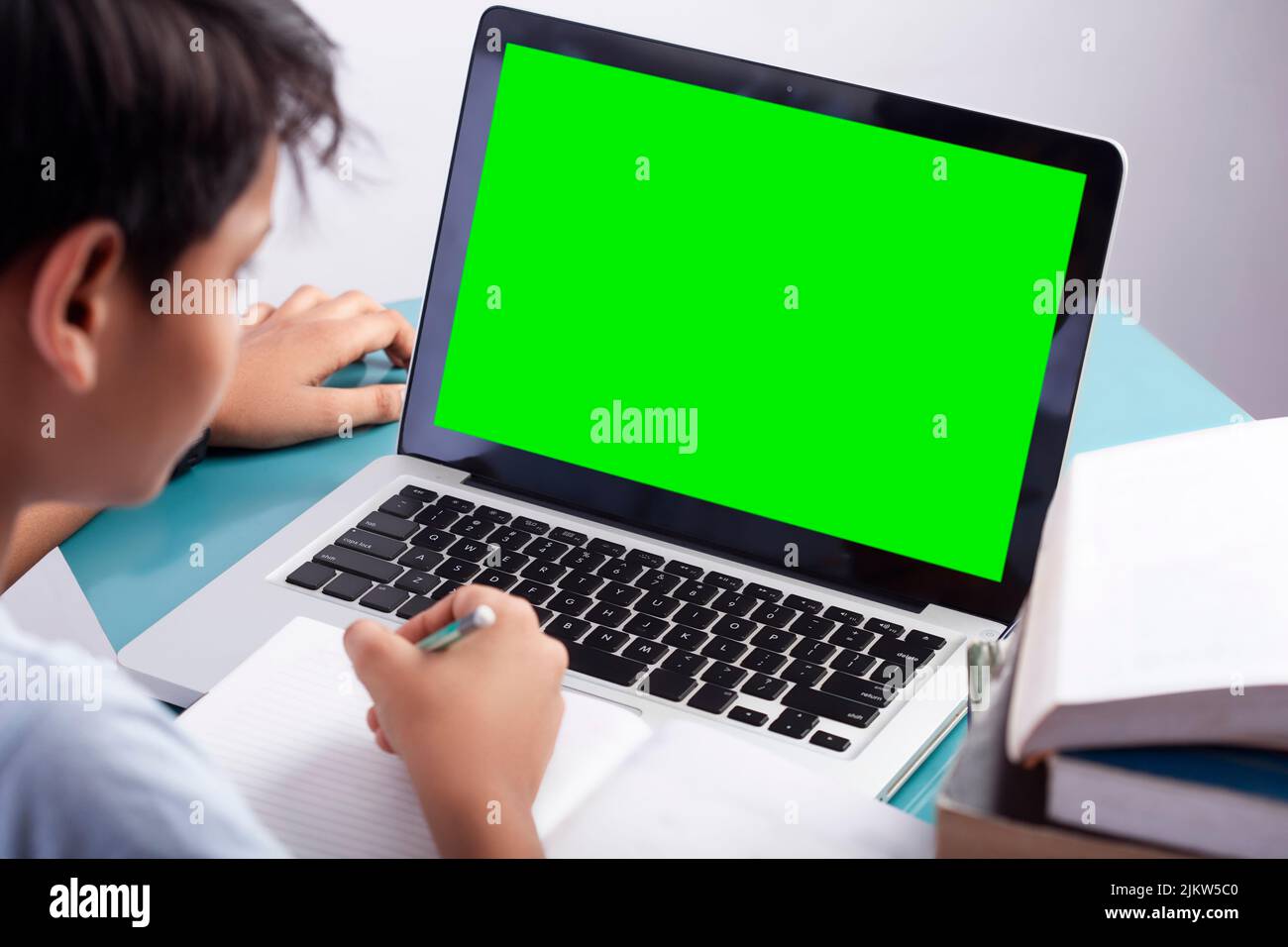 school boy with green screen on laptop studying online class Stock