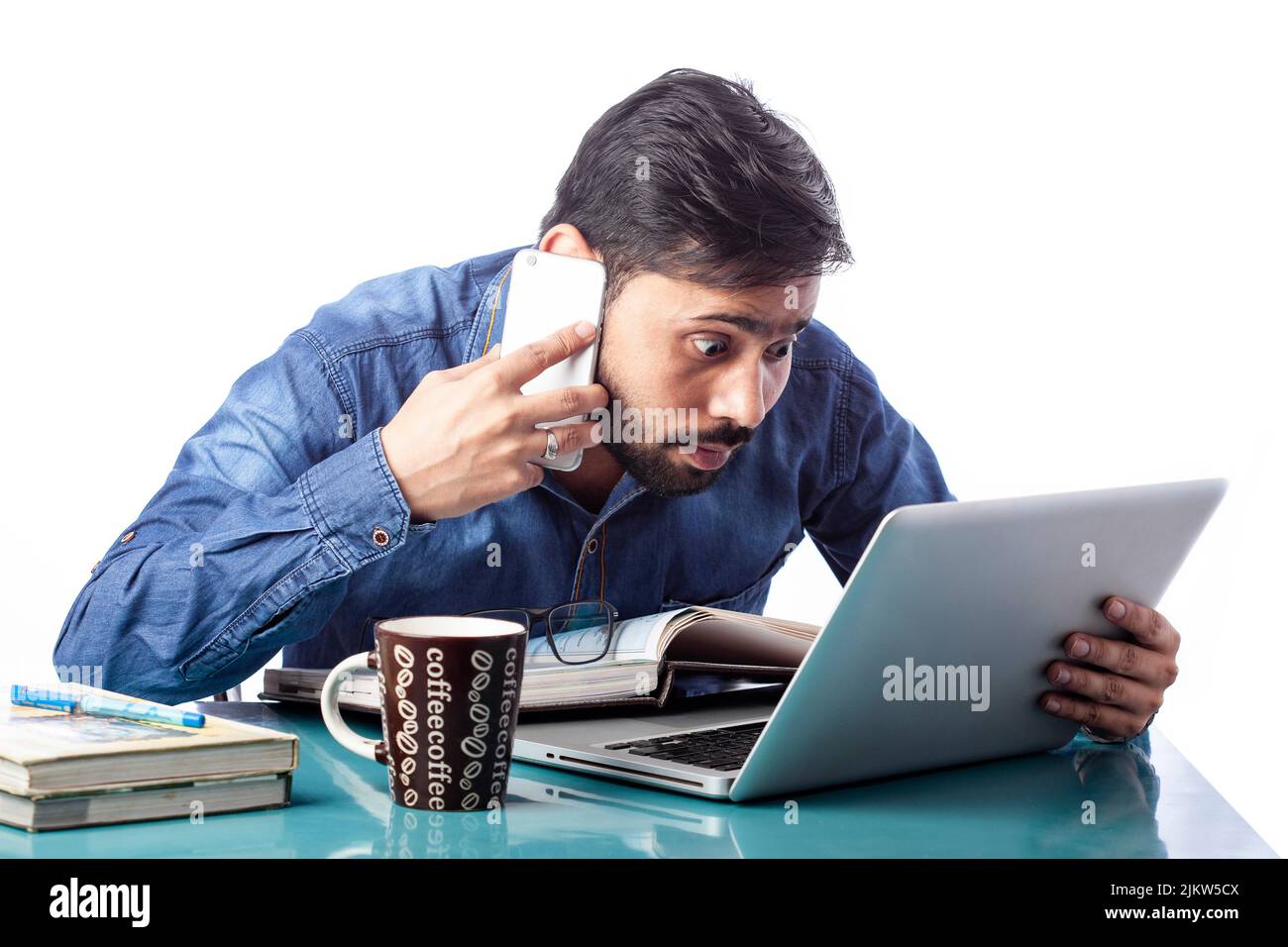 astonished businessman looking at laptop screen while talking on cell phone in isolated white background Stock Photo