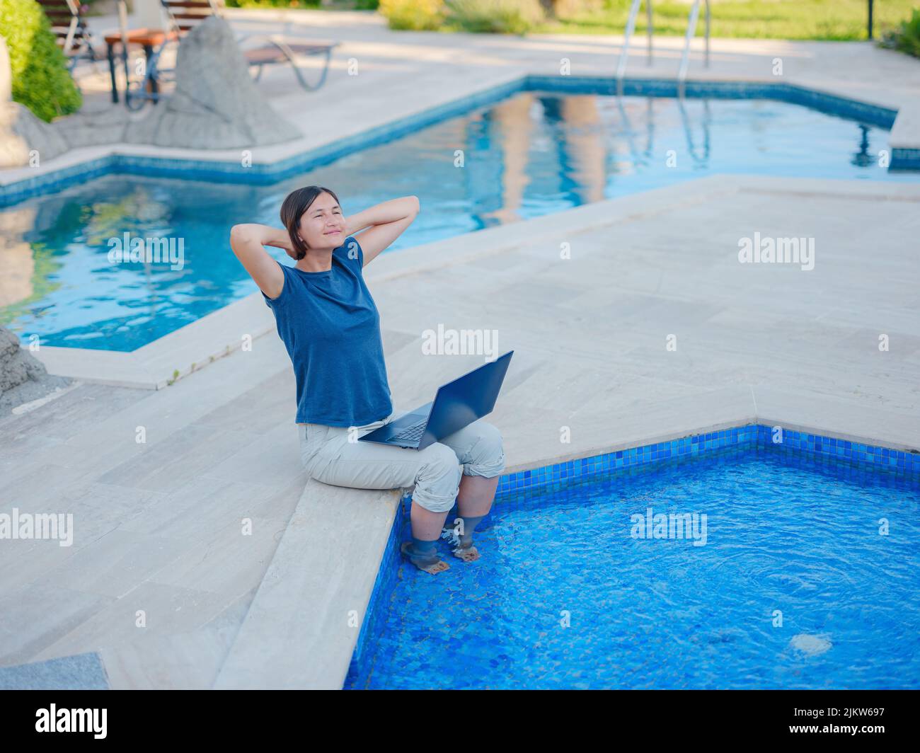 Young business woman working at computer by hotel pool. Young lady ...