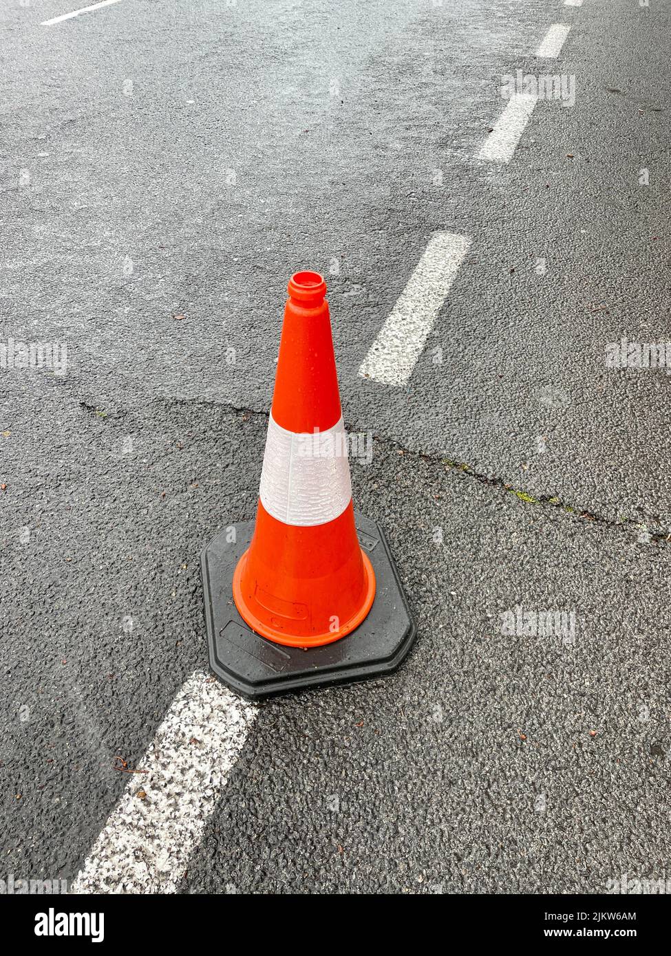 A vertical shot of an orange traffic cone on the road Stock Photo