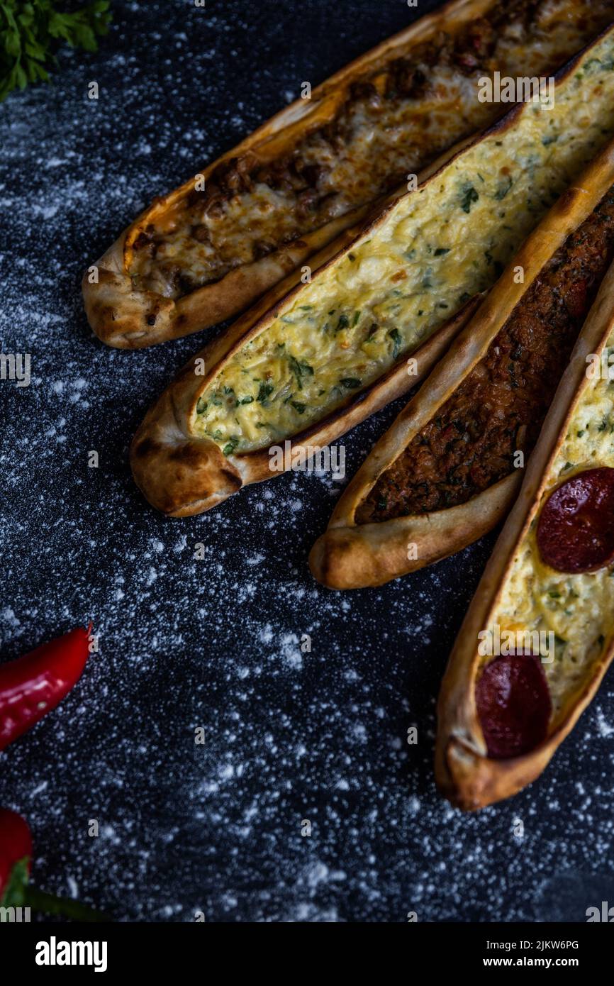 A vertical shot of four sticks of pide bread with cheese and meat on the black surface with flour Stock Photo