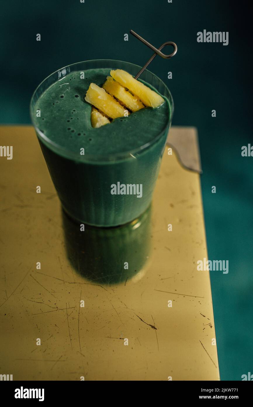 green spirulina smoothie with pineapple on brass, gold table and teal