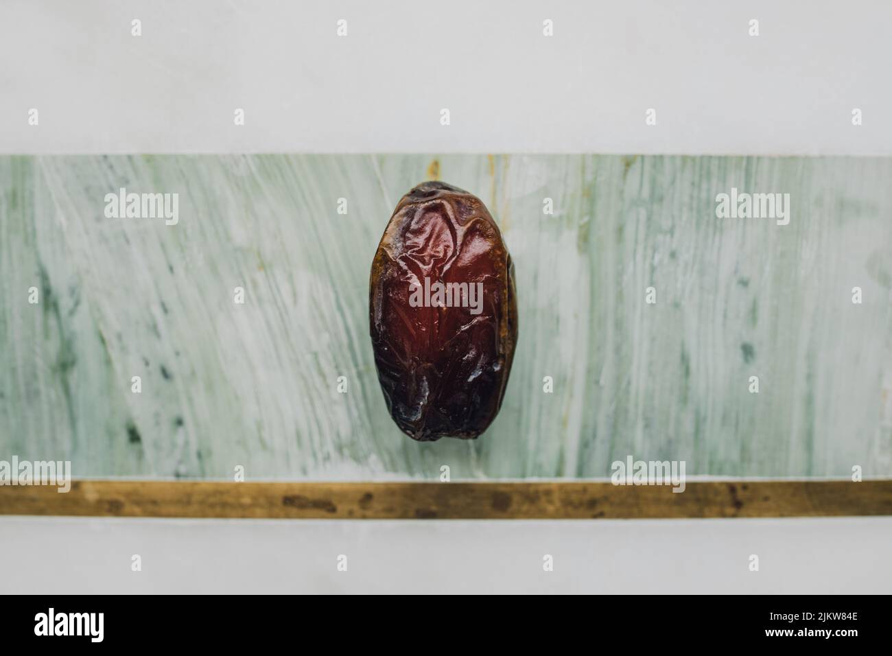 single date, fruit on green, marble, brass cheese board Stock Photo