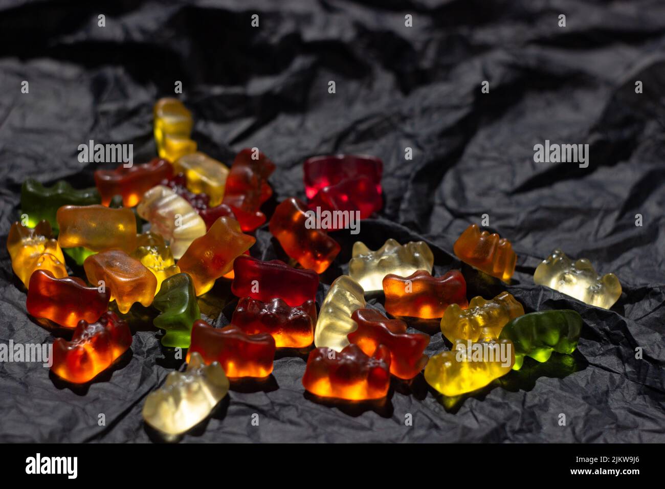 Multi-colored gummy bears lie in a chaotic manner on a black crumpled material Stock Photo