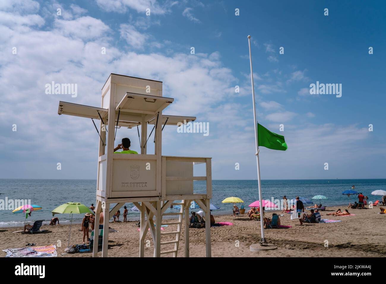 Sea coast safety guard at coastal safety tower, green flag indicating safe conditions for beach visitors. MARBELLA, MALAGA/SPAIN - JULY 21 2022 Stock Photo