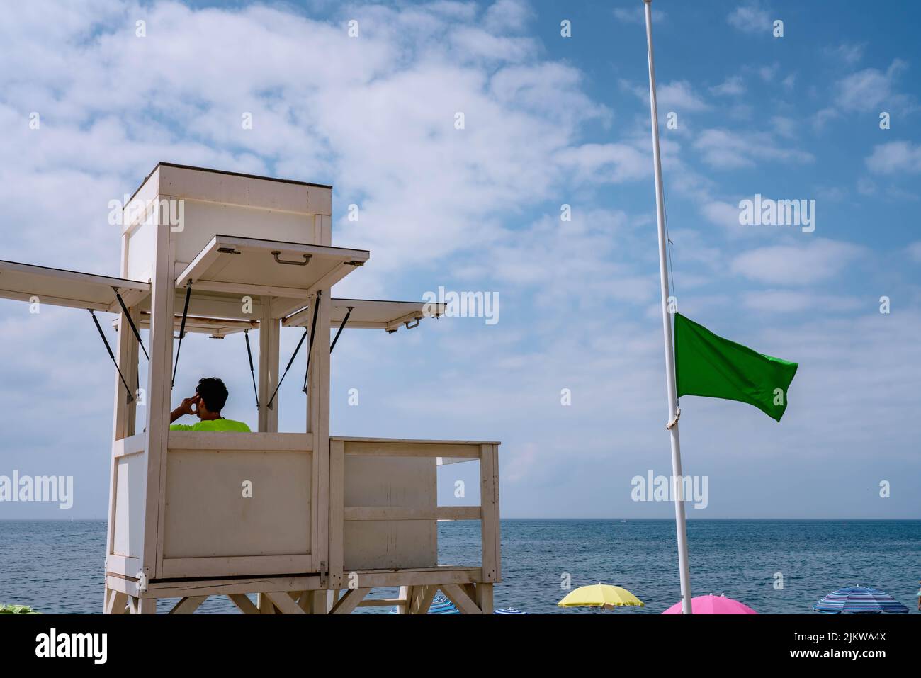 Sea coast safety guard at coastal safety tower, green flag indicating safe conditions for beach visitors Stock Photo