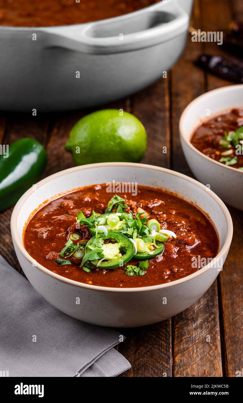 A vertical closeup of a tomato soup with chilis, greens, jalapeno pepper and lime on a wooden table Stock Photo