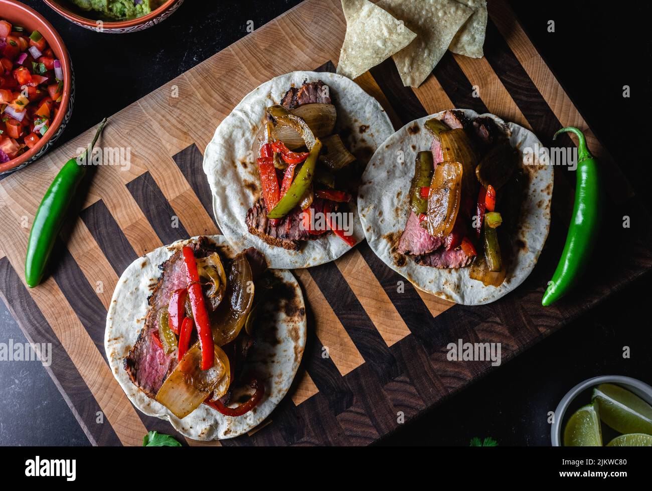 A top view of fajitas on tortillas with grilled steak, peppers, salsa, and jalapenos on a wooden board Stock Photo