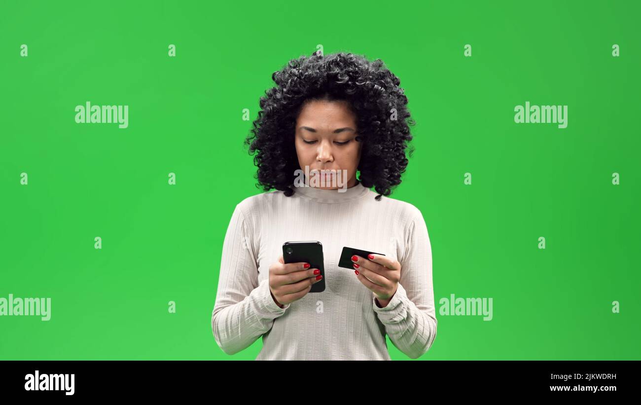 An African American girl with curly hair holds a smartphone and ID card with a green chroma in the background Stock Photo