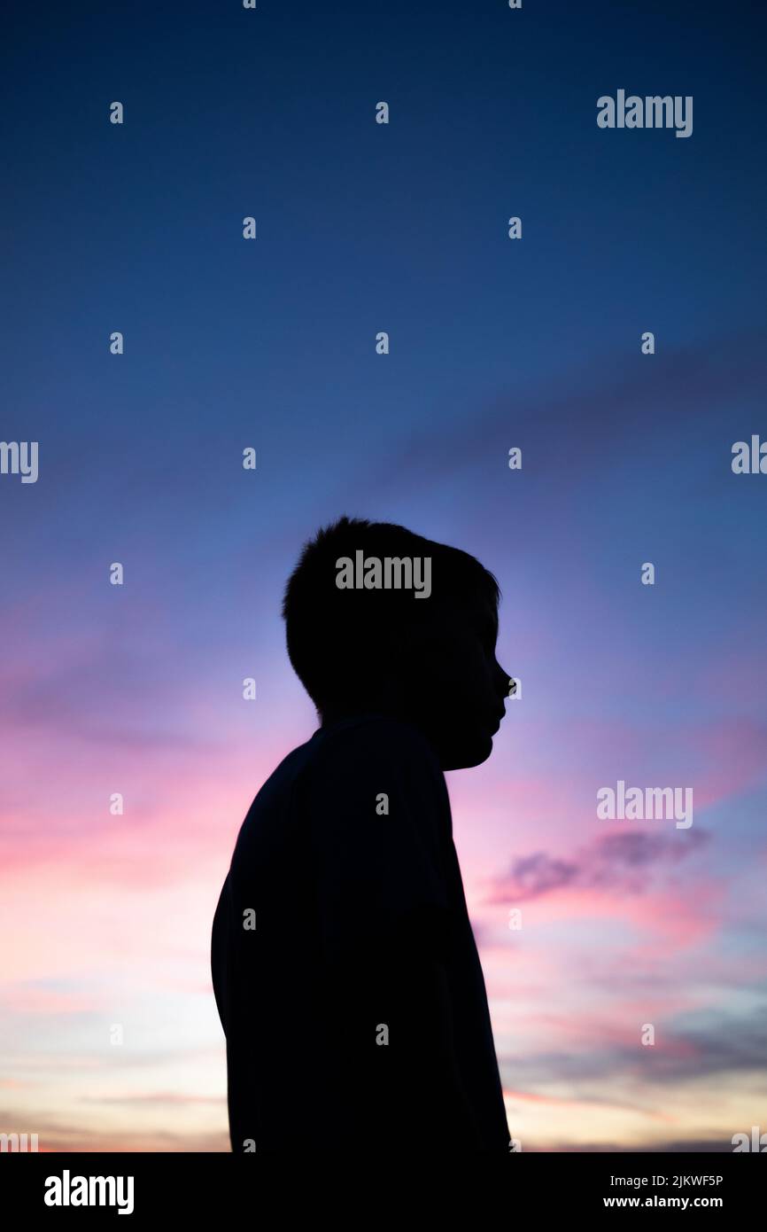 A vertical shot of a side silhouette of a young boy against the sunset view Stock Photo