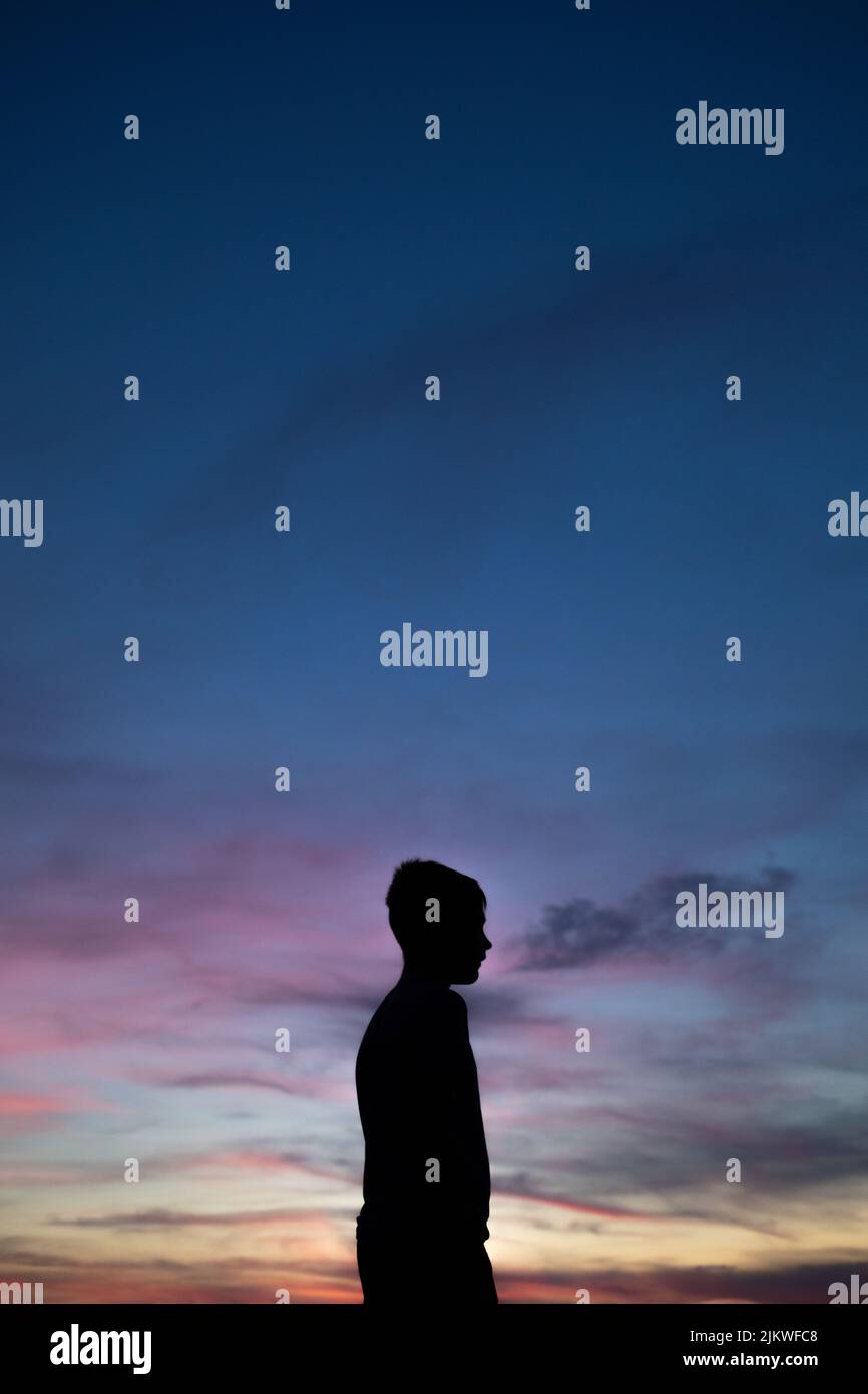 A vertical shot of the side silhouette of a young boy enjoying the sunset view Stock Photo