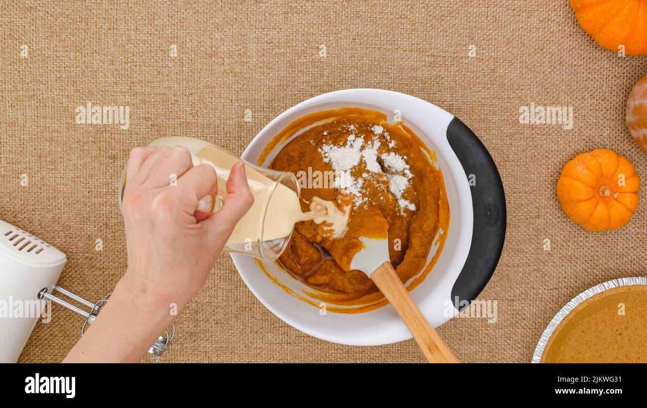 Mixing pumpkin puree, woman hands add evaporated milk in a bowl. Step by step pumpkin pie recipe, close up view from above, copy space Stock Photo