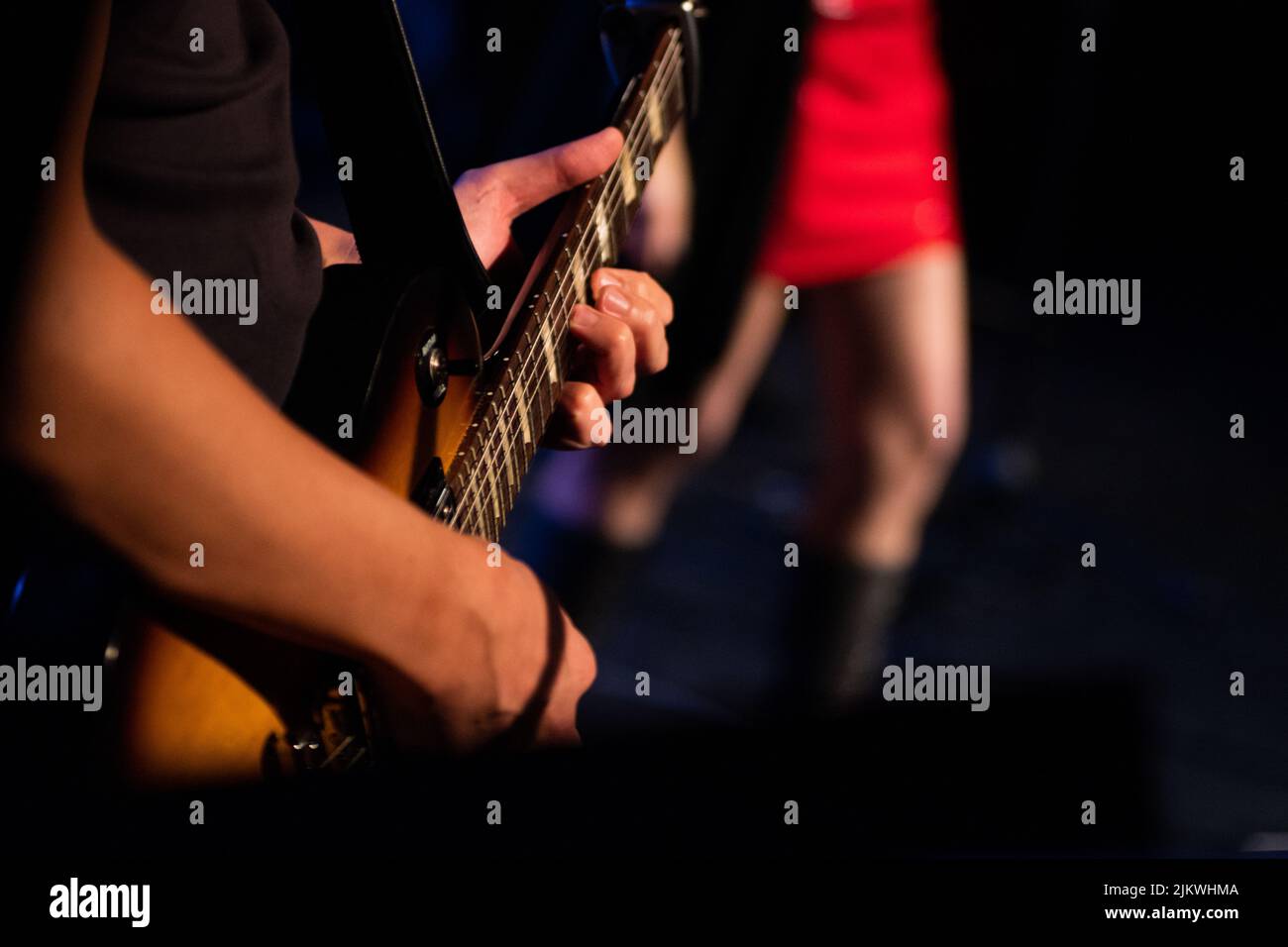 A selective focus shot of a man playing an electric guitar on the stage Stock Photo