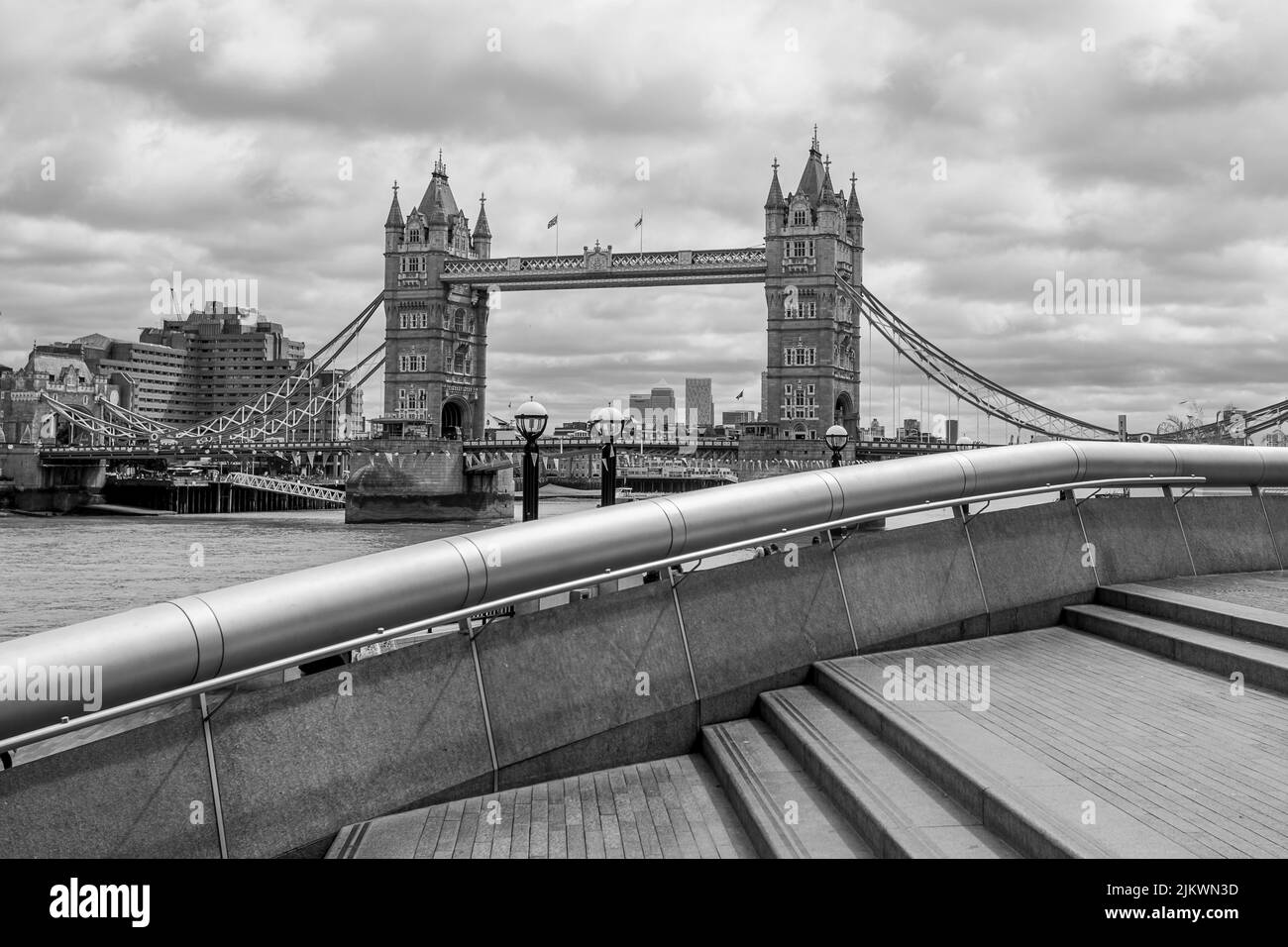 Black and white image of Tower Bridge spanning the River Thames seen over the steps and curved railing of The Scoop in August 2022. Stock Photo