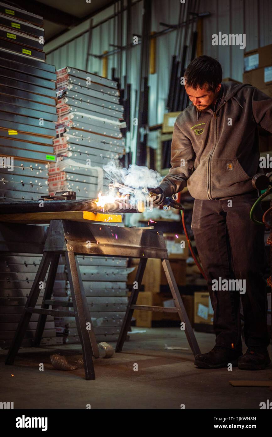 A vertical shot of a male using a cutting torch as bright flame casts