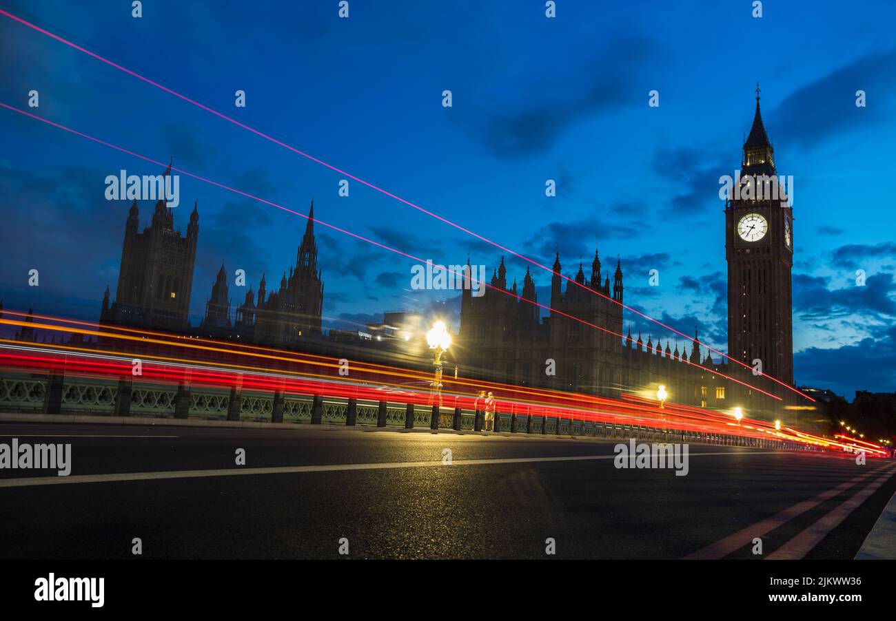 Red traffic trails captured at twilight in July 2022 as vehicles pass Westminster Bridge and towards Big Ben. Stock Photo
