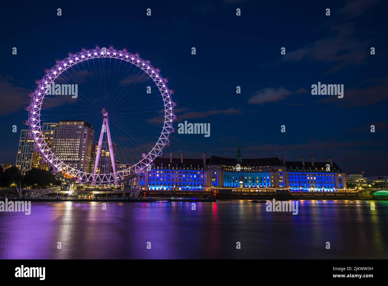 Colourful reflections of the London Eye and London Aquarium seen on the River Thames one evening in July 2022. Stock Photo