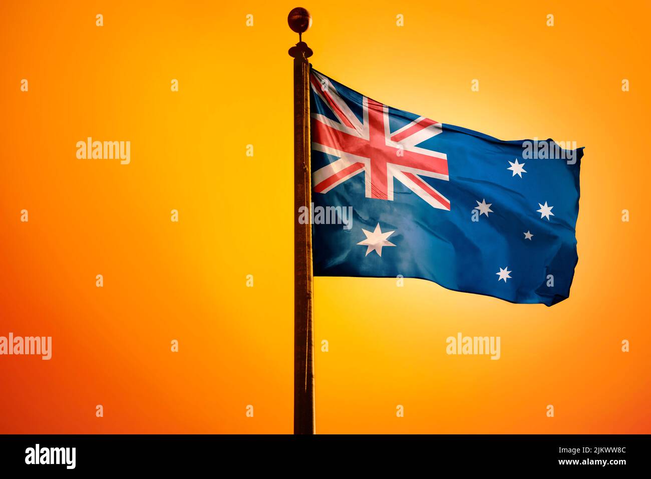 A digital illustration of the flag of Australia waving against a bright yellow sky Stock Photo