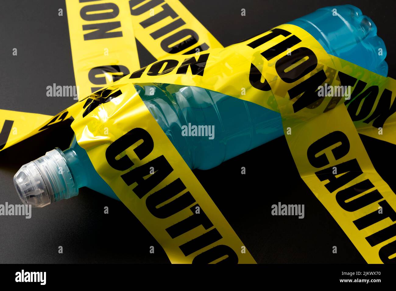 Sugary sports drink plastic bottle wrapped in yellow caution tape concept for dangerous liquid candy, dietary warning about beverages with high sugar Stock Photo