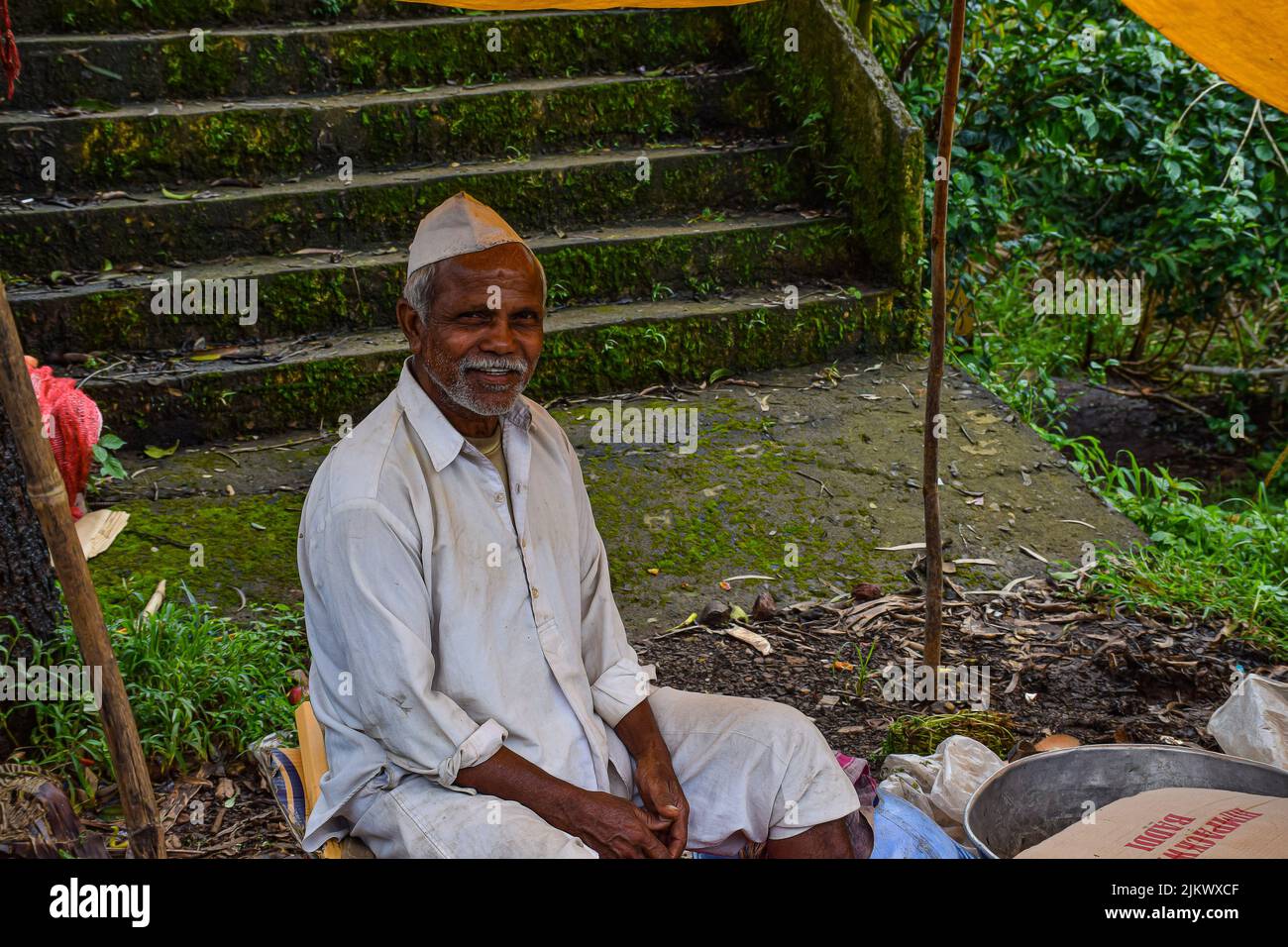 Kolhapur ,India- September 15th 2019; stock photo of 50 to 60 age group Indian man wearing white shirt, pant and cap, selling farm, fresh fruits in th Stock Photo