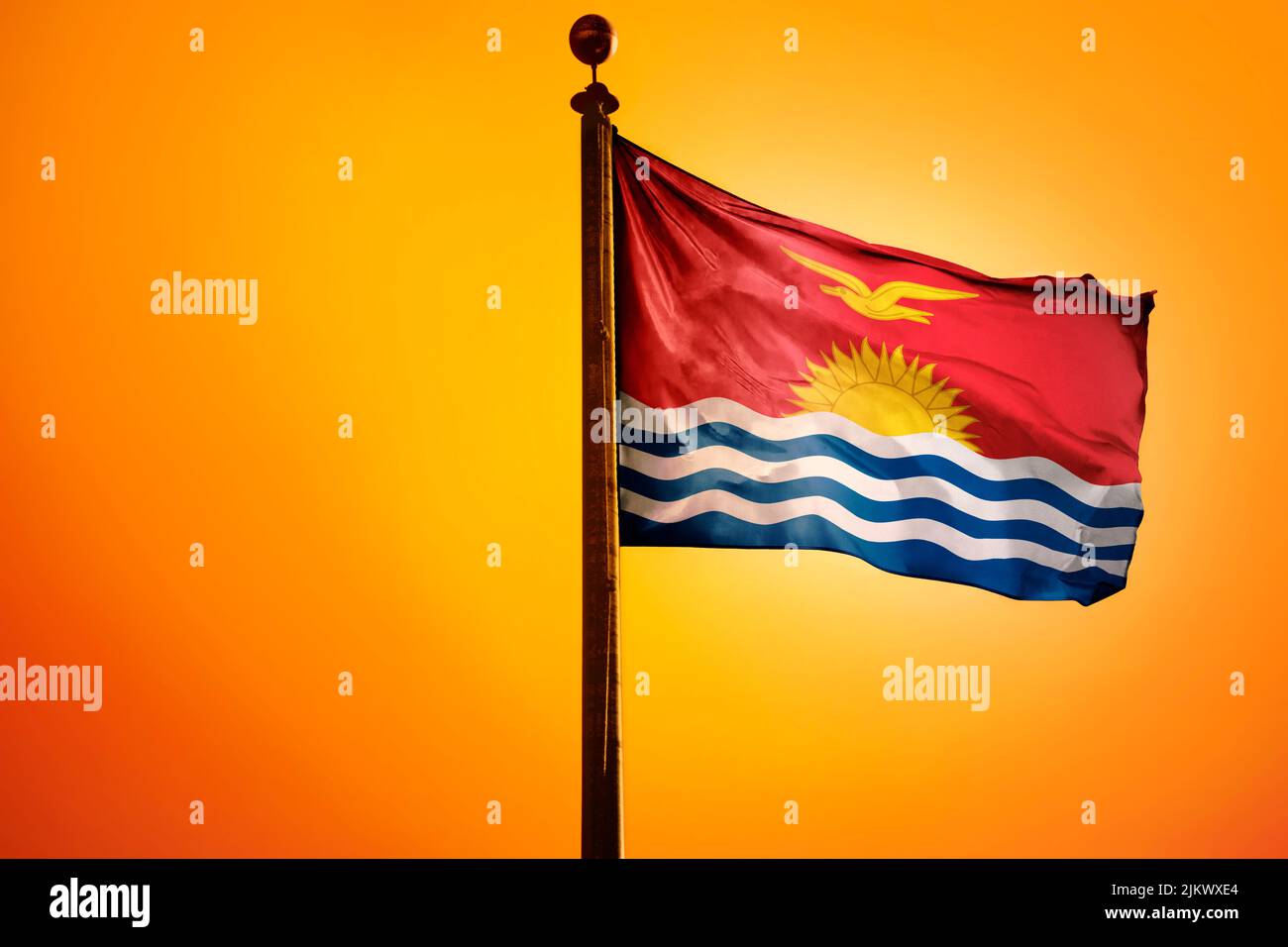 The national flag of Kiribati on a flagpole isolated on an orange background Stock Photo