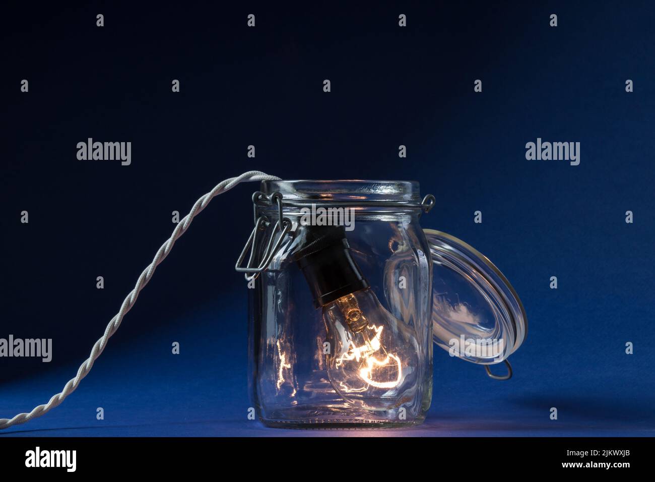 A lit incandescent light bulb enters a canning jar against a black and