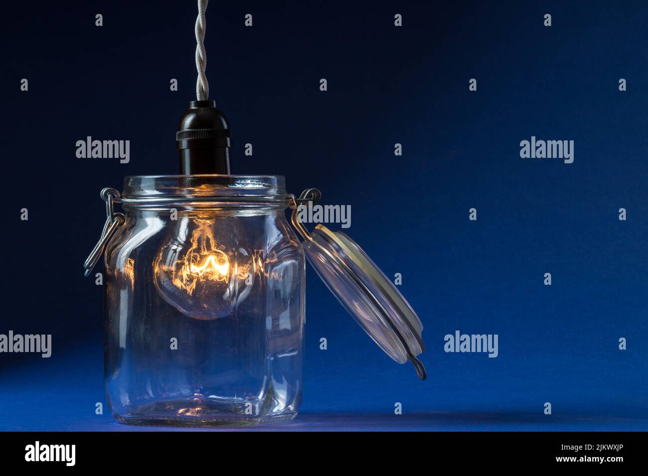 A lit incandescent light bulb enters a canning jar against a black and