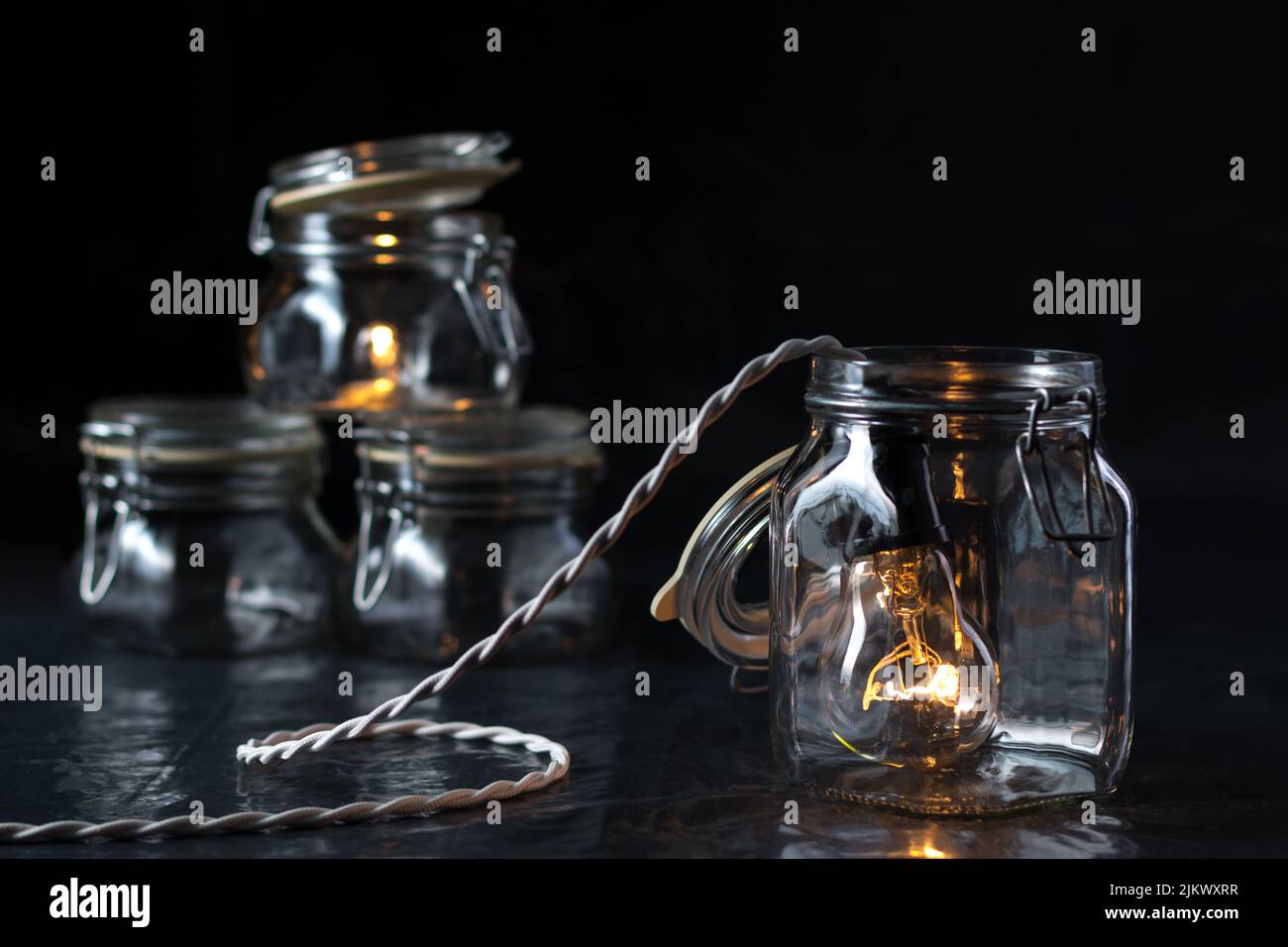 A lit incandescent light bulb enters a canning jar against a black