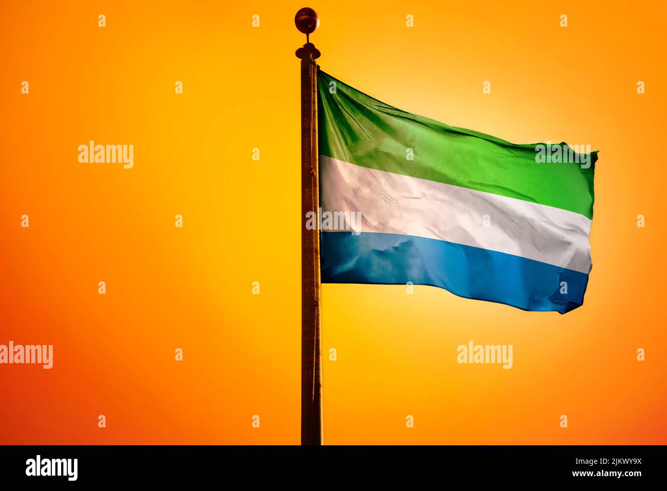 The national flag of Sierra Leone on a flagpole isolated on an orange ...