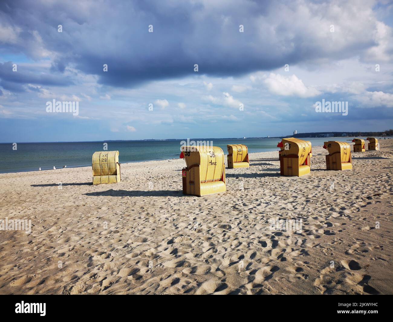 A scenic view of benches on the sandy beach against a blue seascape under a cloudy sky on a sunny day Stock Photo