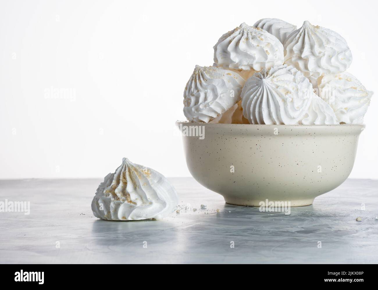 close-up of meringue sprinkled with nut crumbs in a white plate on a gray background with copy space, selective focus. home cooking. Postcard for conf Stock Photo