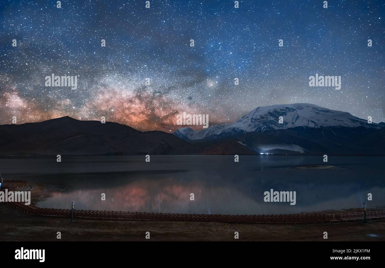 A beautiful view of a lake surrounded by hills under the night sky with Milky Way galaxy Stock Photo