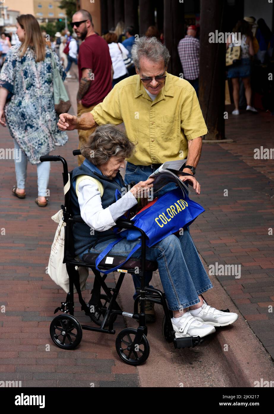 An elderly woman and her husband use a transport chair, or transport wheelchair, as they visit an outdoor arts festival in Santa Fe, New Mexico. Stock Photo