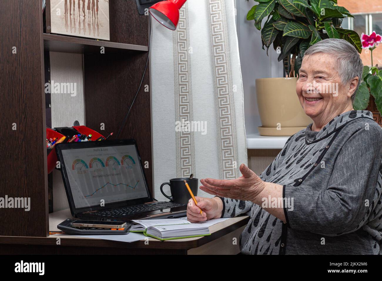funny, smiling senior business woman, discussing work issues with someone, joking, sitting at workplace near laptop, selective focus, using technology Stock Photo