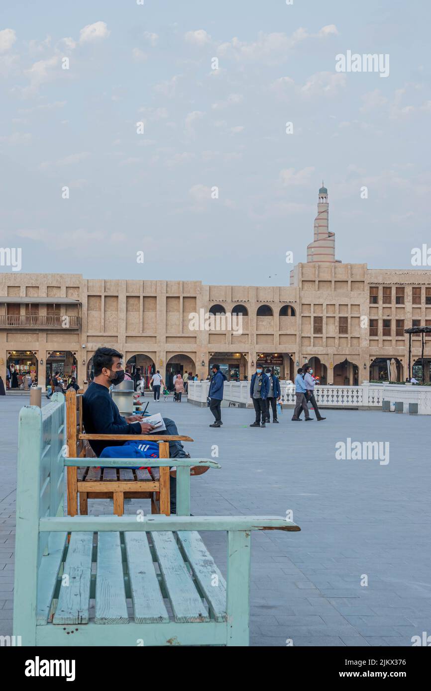 Vertical shot of a guy sitting on a bench while sketching in Souq Waqif Doha, Qatar Stock Photo