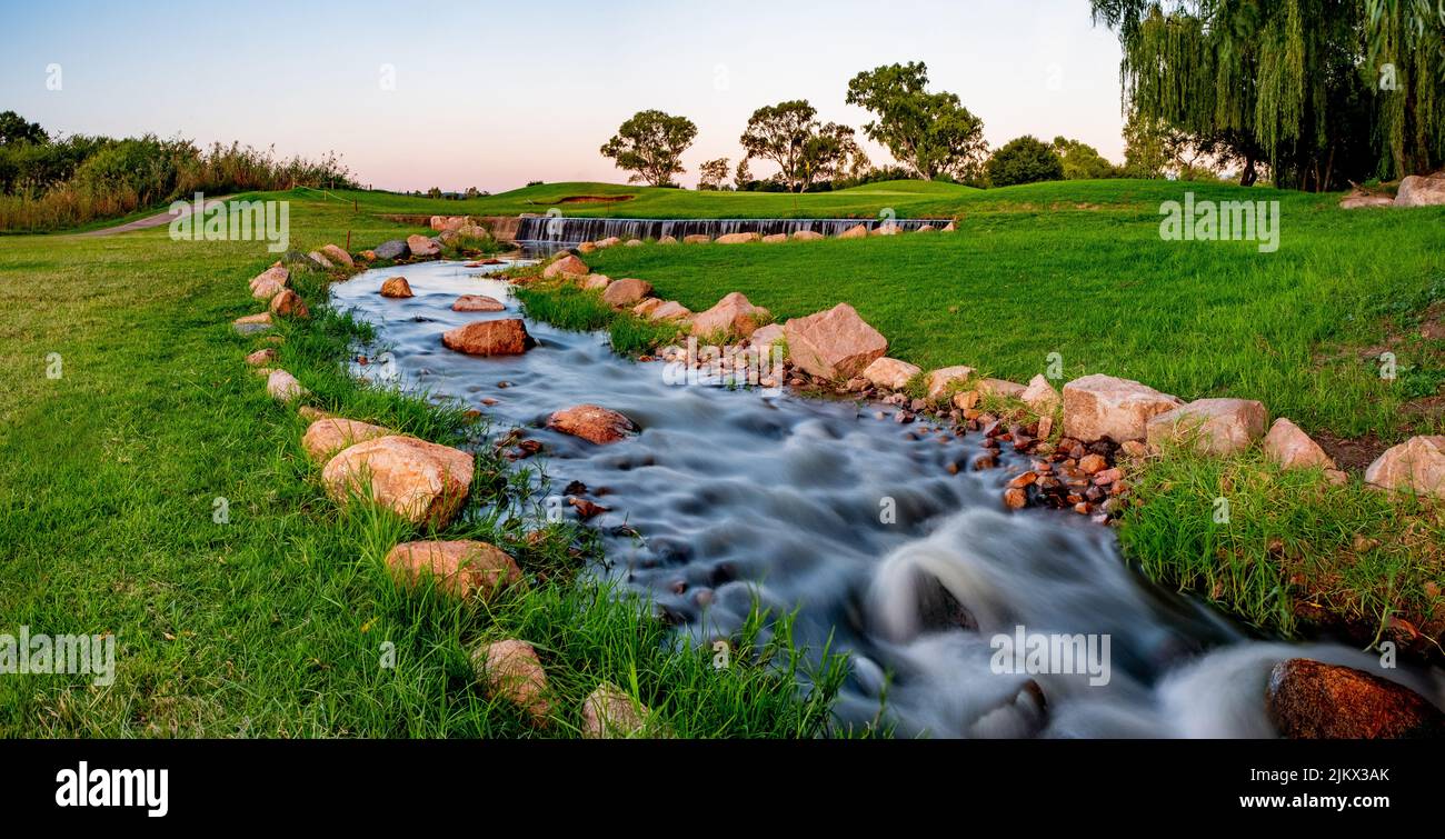 A natural landscape view of a river flowing in the green untouched field Stock Photo