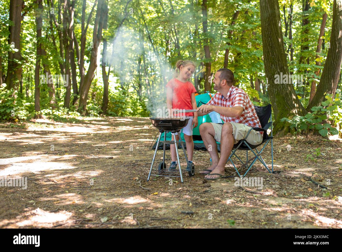 A Caucasian father and a daughter preparing a barbecue at a family picnic in the forest Stock Photo