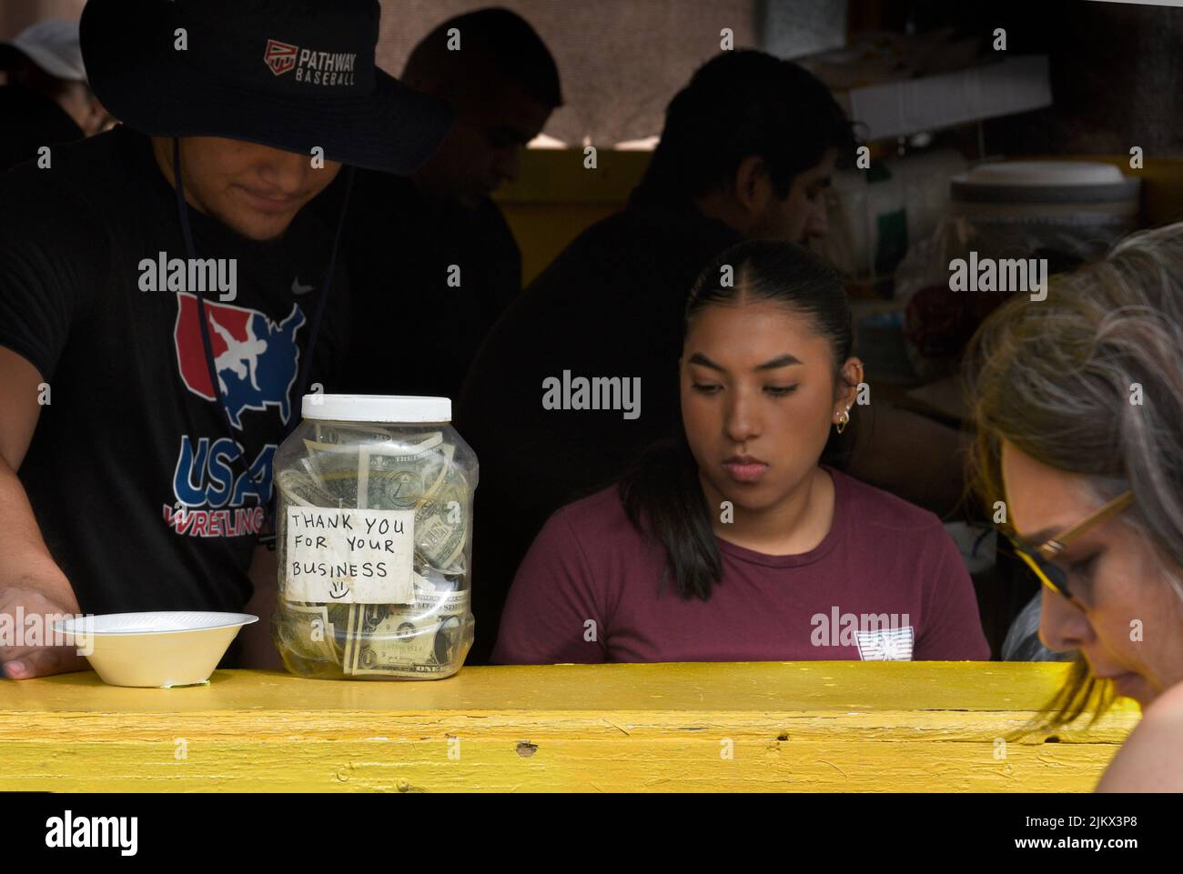 A young hispanic woman takes lunch orders at her food vendor booth at the annual Spanish Market art festival in Santa Fe, New Mexico. Stock Photo